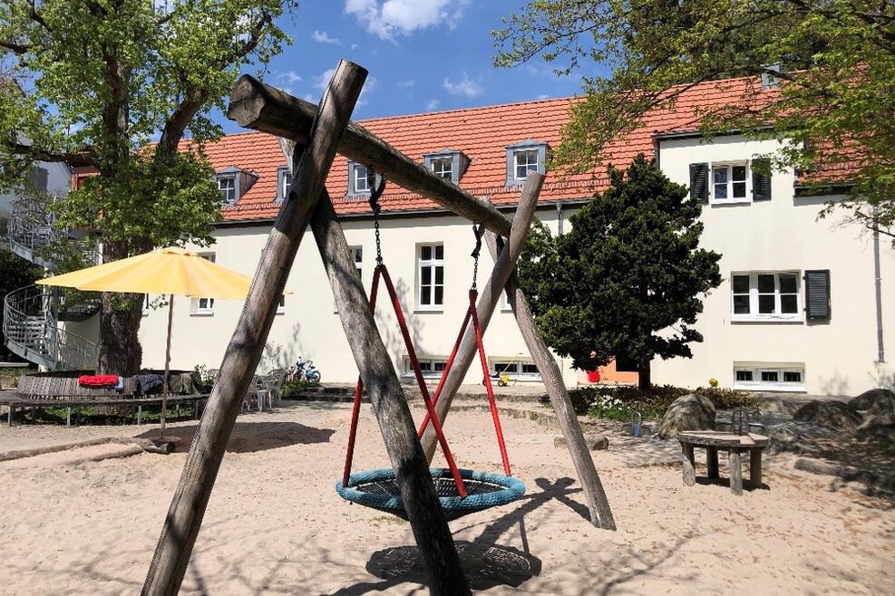 Der Spielplatz mit Sandkasten und Korbschaukel.