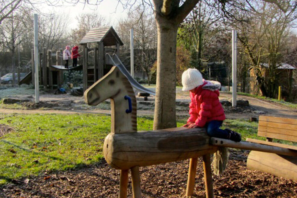 Auf dem Spielplatz steht ein Holzpferd zum Klettern.