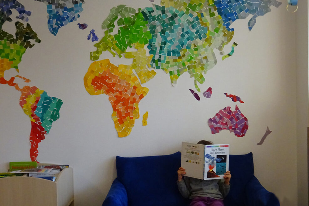 Im Lesebereich klebt die Weltkarte aus verschieden farbigen Papierstückchen gebastelt an der Wand.