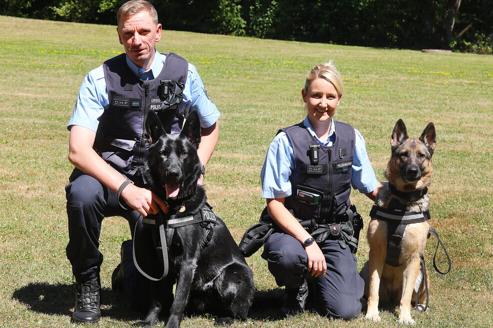 Zwei Vollzugsbeamte knien neben ihren Hunden auf dem Boden.