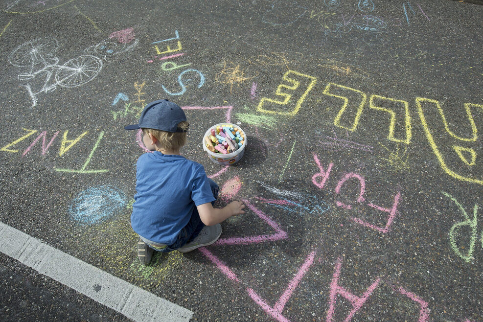 Ein Kind malt mit Straßenkreide auf der Theodor-Heuss-Straße