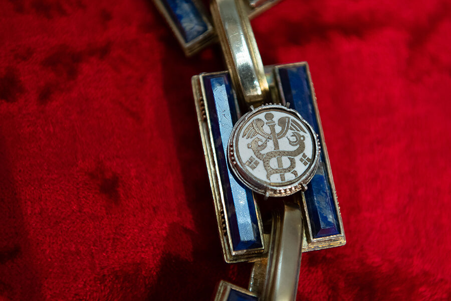 Das Foto zeigt ein Kettenemblem mit dem Hermesstab, der sinnbildlich für den Handel steht.