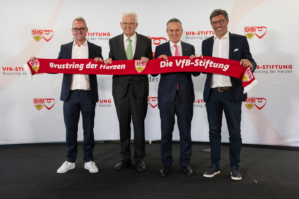 Alexander Wehrle, Ministerpräsident Winfried Kretschmann, OB Nopper und Claus Vogt halten eine großen Fan-Schal mit der Aufschrift „Brustring der Herzen. Die VfB-Stiftung.".