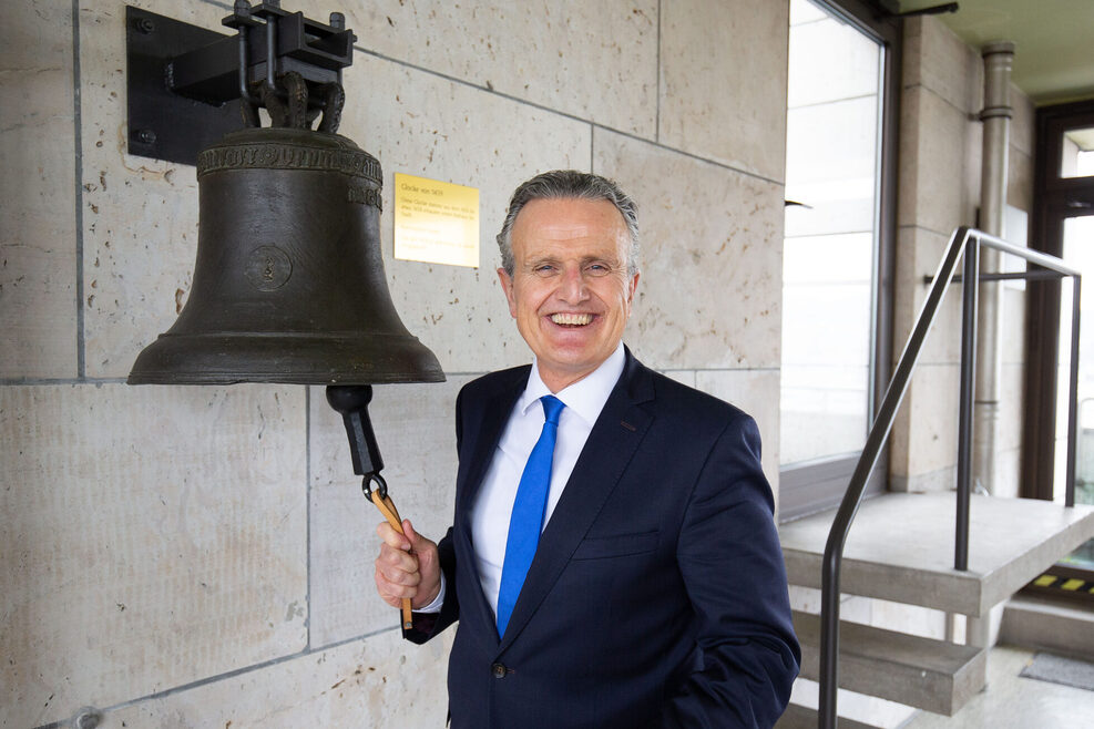 Oberbürgermeister Dr. Frank Nopper steht lächelnd vor einer Glocke im Rathausturm