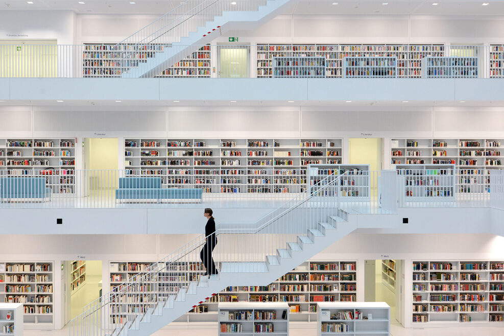 Eine Frau läuft eine weiße Treppen hinunter. Im Hintergrund sind viele Bücher in weißen Regalen zu sehen.