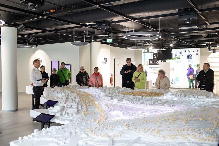 Im Ausstellungsraum zu Stuttgart Rosenstein stehen rund um das große Modell Besucher. Ein Mitarbeiter erklärt ihnen, worum es bei Stuttgarts größtem Städtebauprojekt geht.
