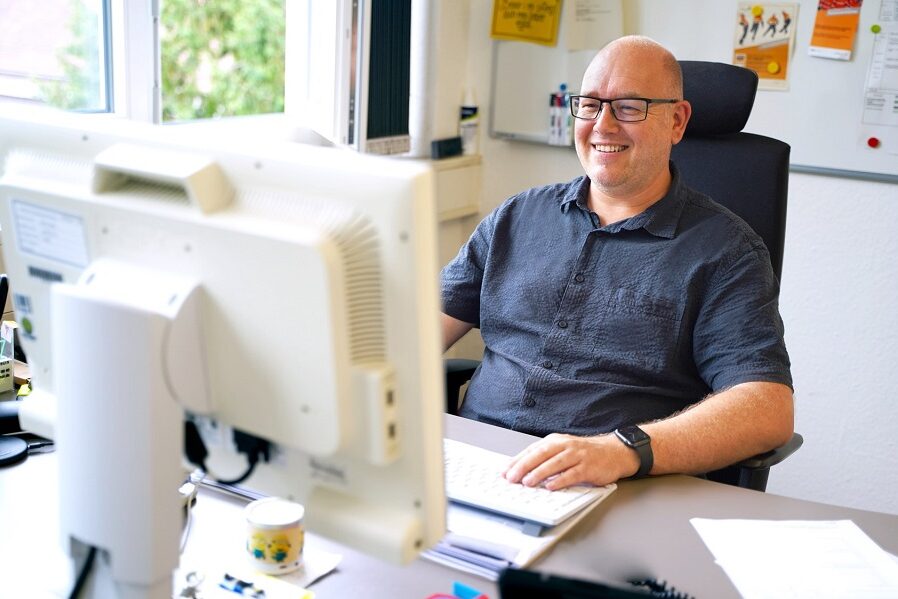 Eine Person sitzt im Büro an einem Schreibtisch und schaut auf einen Bildschirm.