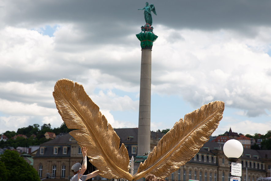 Goldene Engelsflügel vor einer Statue auf einer am Schlossplatz