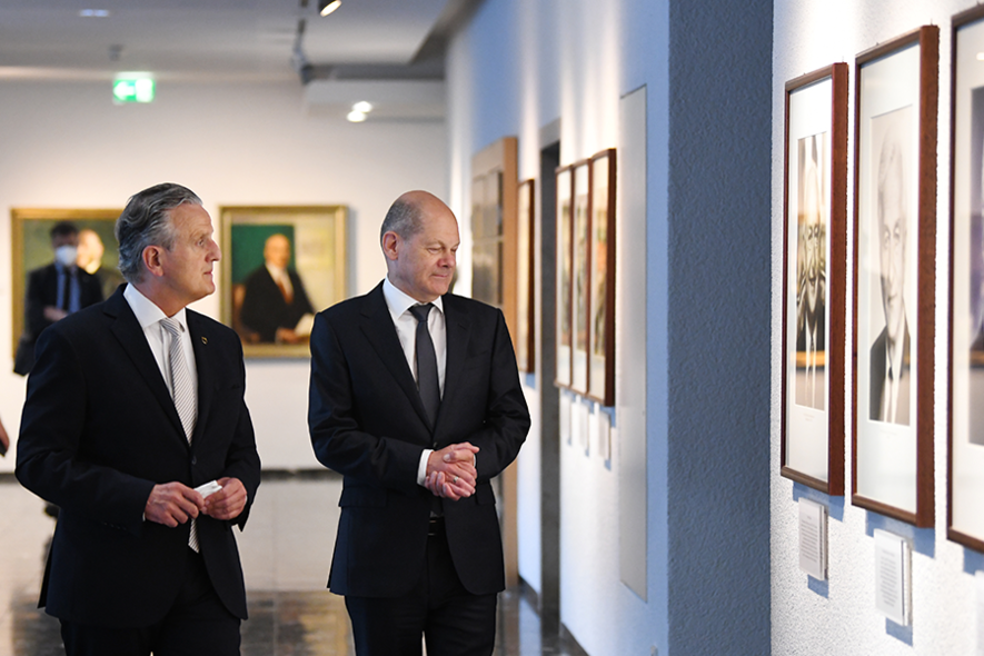 Oberbürgermeister Frank Nopper und Bundeskanzler Olaf Scholz schauen Bilder an einer Wand an.