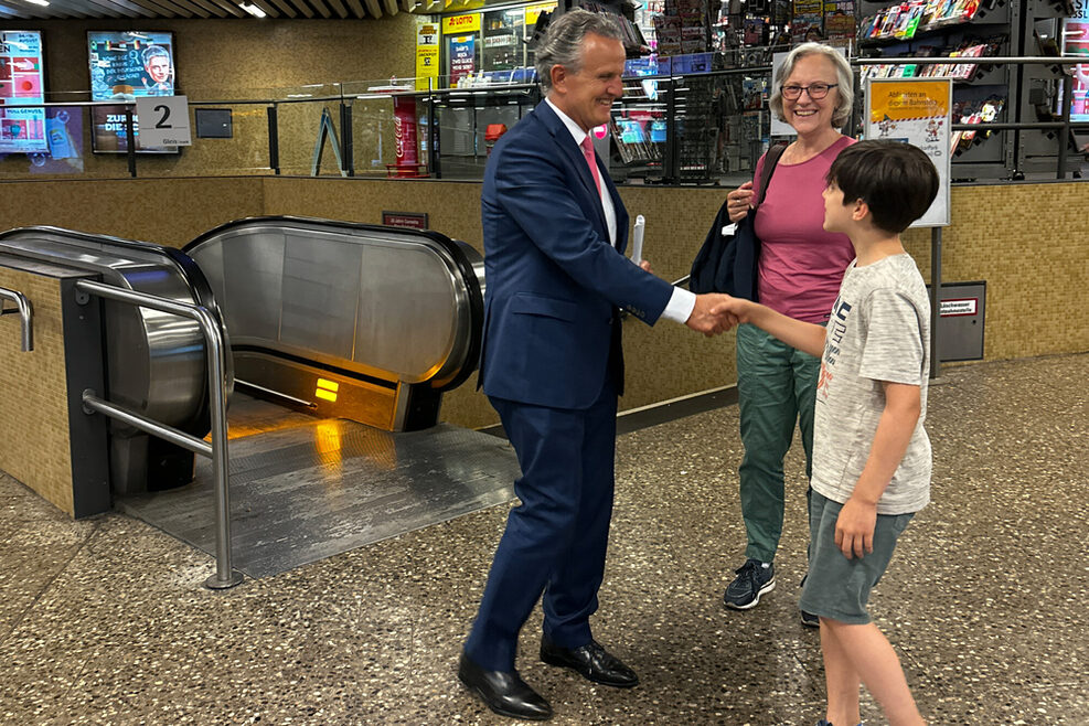 Ein Mann schüttelt einem Jungen die Hand. Daneben steht eine ältere Dame und lächelt.