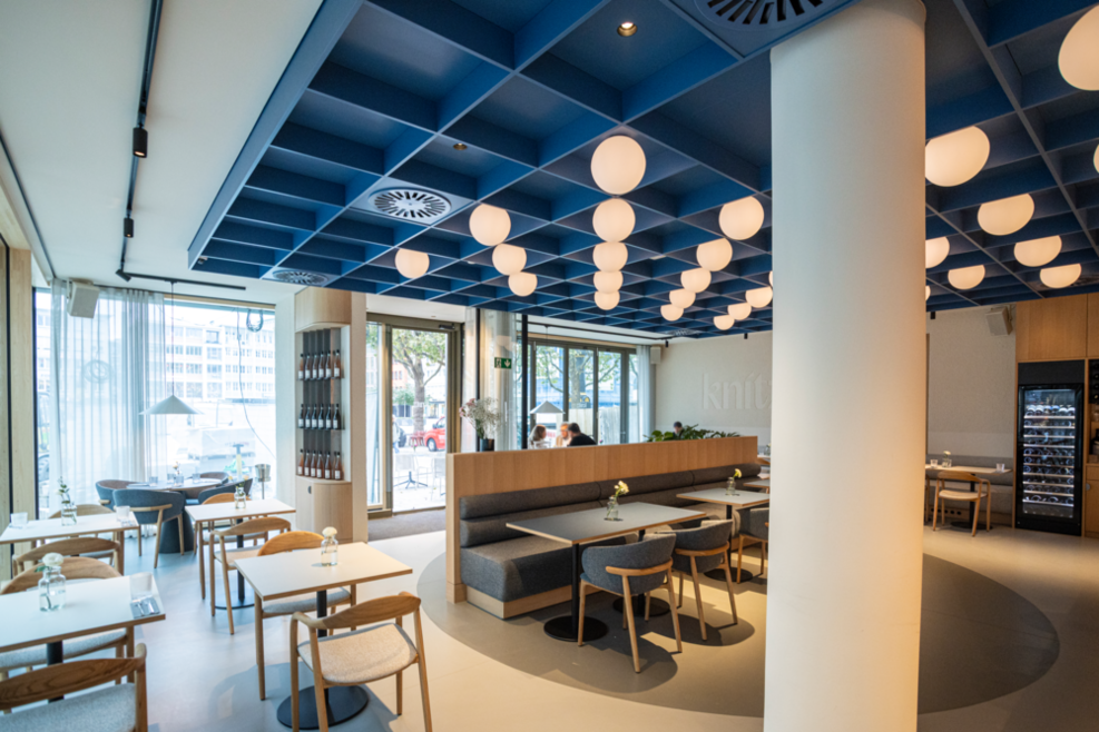 Innenraum des Restaurant knitz im Haus des Tourismus am Marktplatz in Stuttgart. Kugelförmige Deckenleuchten und helle Holzmöbel mit grauen Polstern schaffen eine gemütliche Atmosphäre.