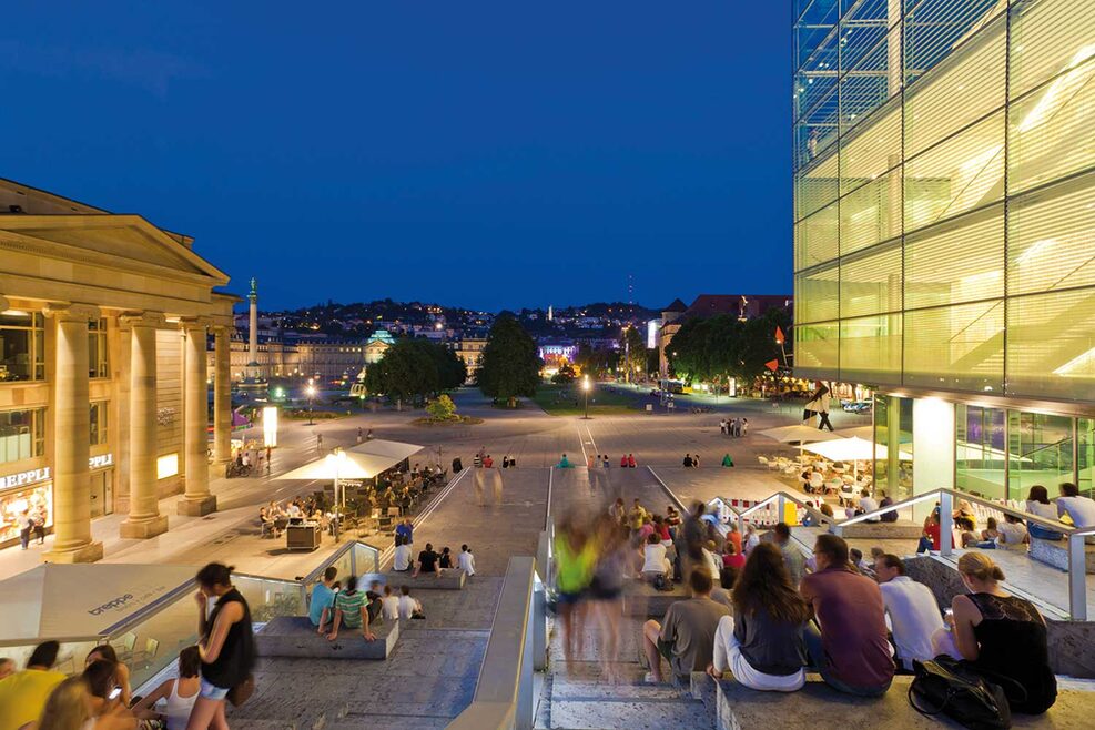 Menschen sitzen auf einer Treppe und blicken auf den Schlossplatz.