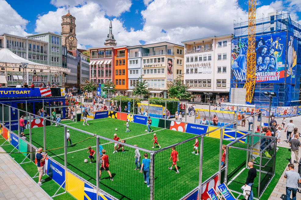 Fan Zone auf dem Marktplatz mit kleinem Fußballfeld, auf dem Kinder Fußball spielen.