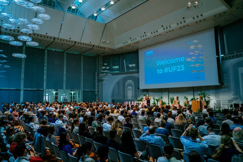 Zahlreiche Menschen sitzen in einem abgedunkelten Saal im Haus der Wirtschaft und richten ihre Aufmerksamkeit in Richtung Bühne bei der Urban Future Conference 2023 in Stuttgart.
