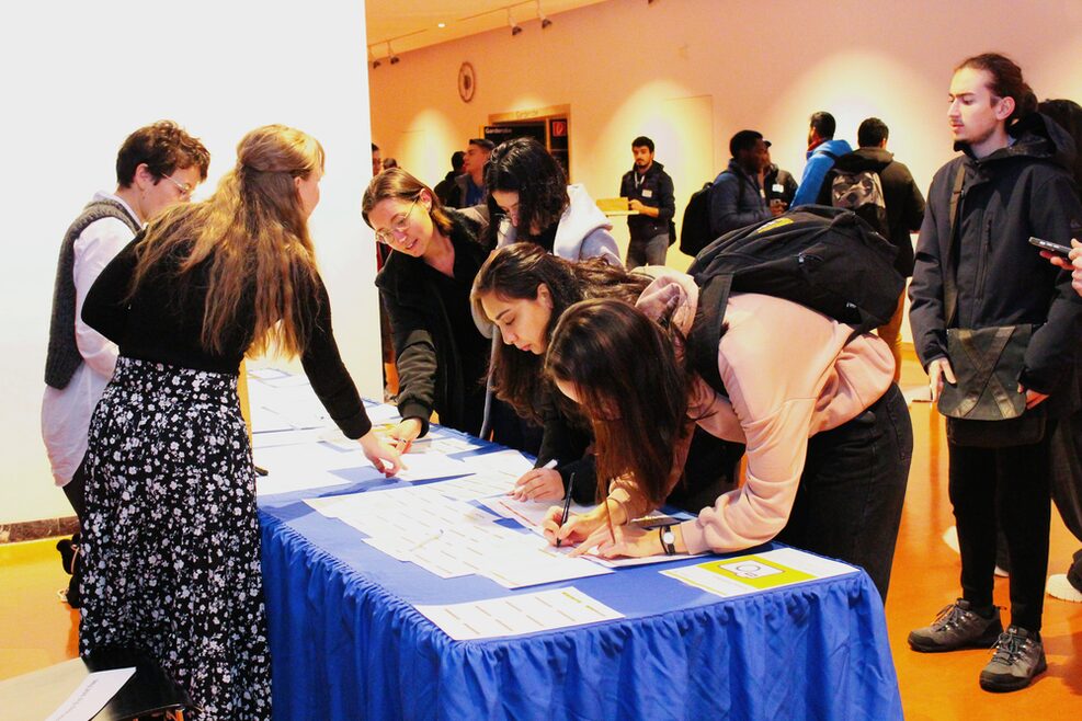 Eine Gruppe Stundenten trägt sich an einem Tisch in eine Liste ein.