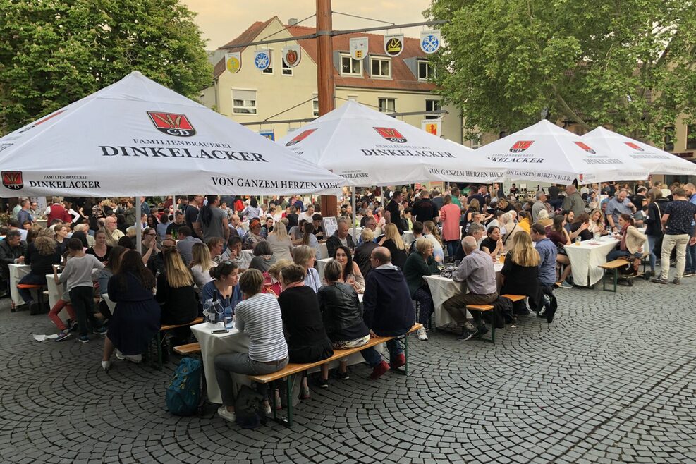 Viele Menschen sitzen an Bierbänken auf einem Marktplatz.