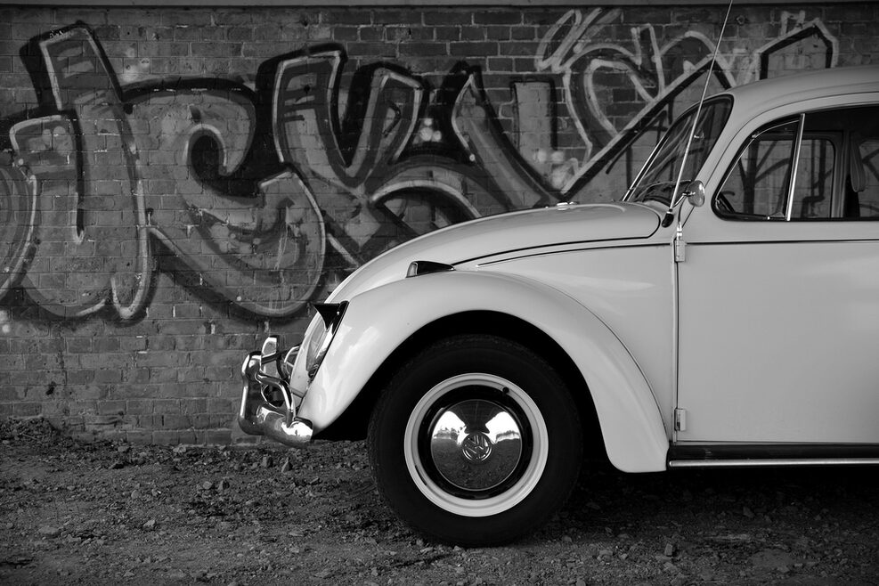 Ein schwarz-weiß Bild mit einem VW-Käfer, der vor einer Graffity-Wand steht.