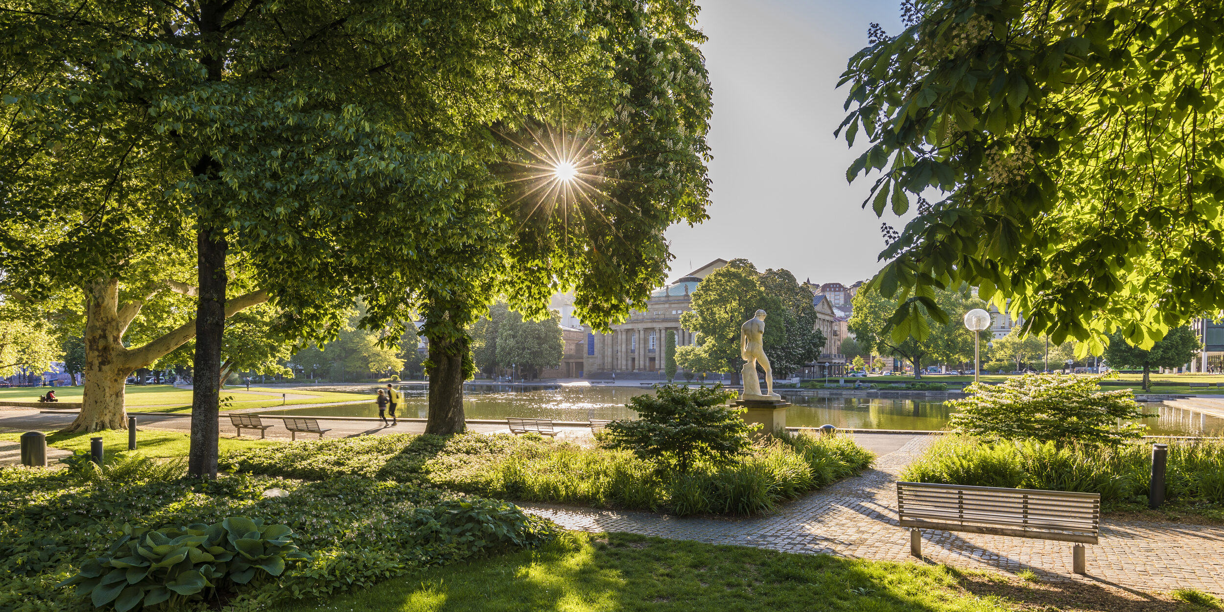 Das Foto zeigt den Eckensee mit Staatsoper an einem sonnigen Sommertag. Auf dem Bild sind ebenfalls Jogger abgebildet.