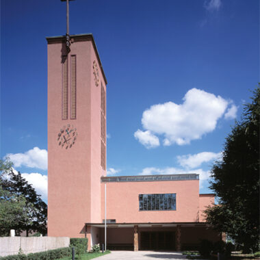 Eine ocker-rote moderne Kirche vor blauem Himmel.
