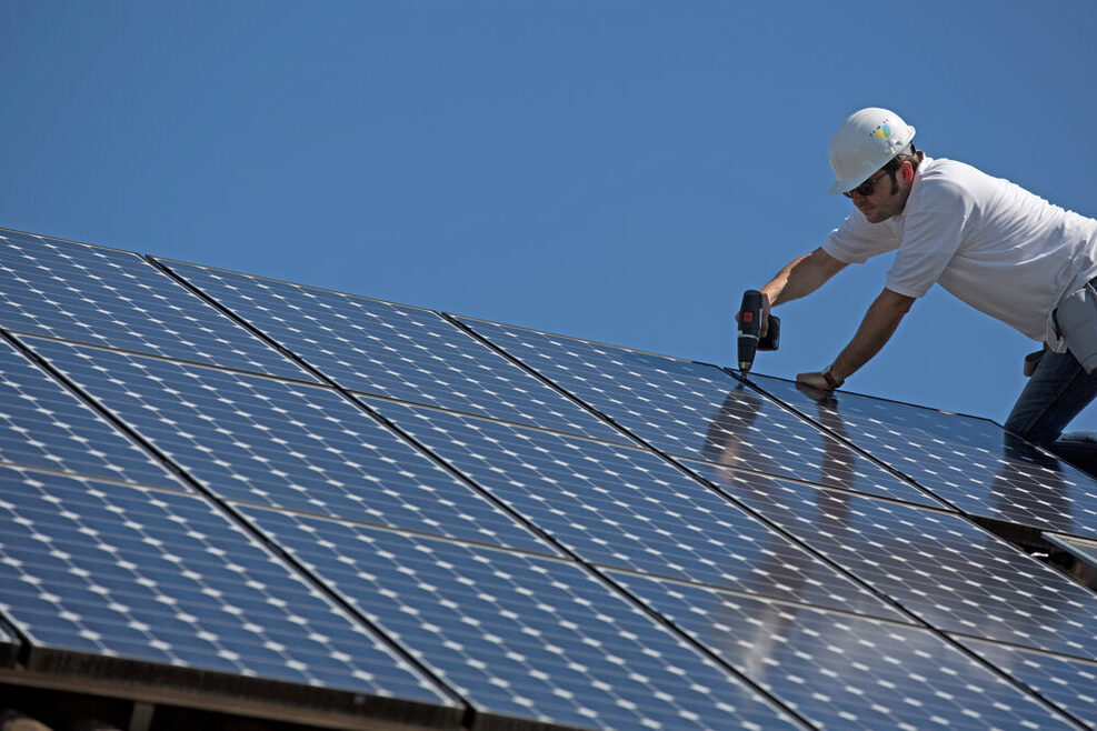 Ein Mann befestigt Solarpanelen auf einem Dach.
