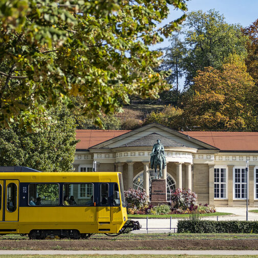 Eine gelbe Stadtbahn fährt vor dem Kursaal vorbei.