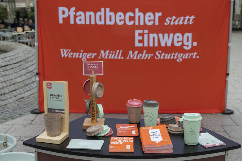 Auf einem Tisch stehen recyclebare ToGo-Becher und es liegen Flyer und Postkarten darauf. Im Hintergrund ist ein Banner der Kampagne "Sauberes Stuttgart" zu sehen.