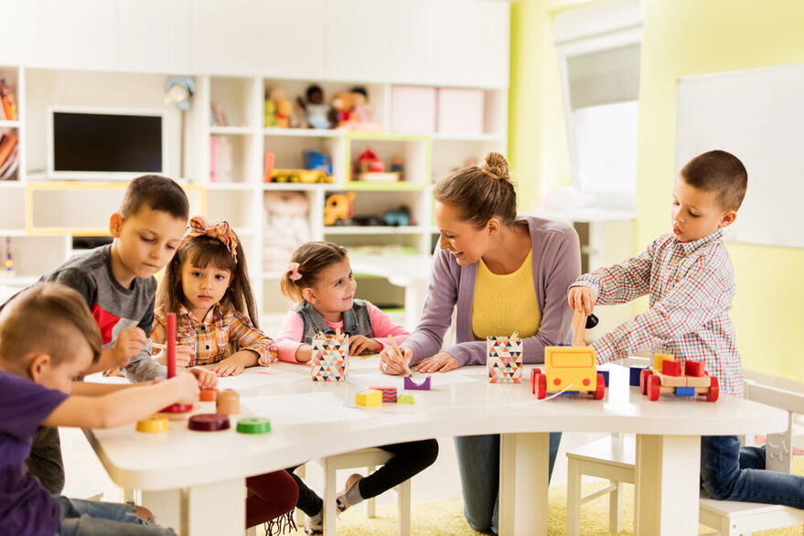 Eine Erzieherin sitzt mit Kindern an einem Tisch.