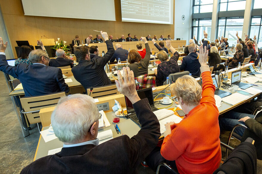 Abstimmung im Gemeindrat: Stadträte heben einen Arm nach oben.