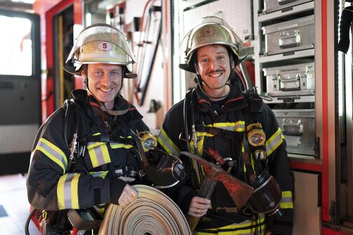 Zwei Feuerwehrleute lachen in die Kamera