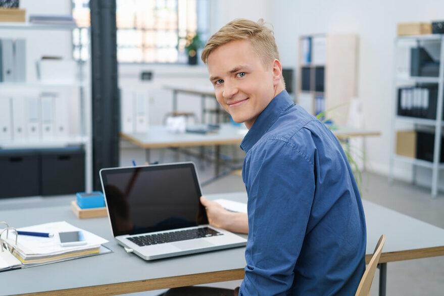 Freundlicher junger Geschäftsmann arbeitet am Laptop.