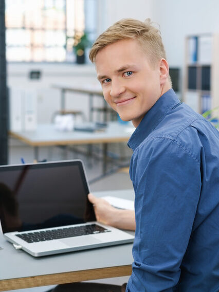 Freundlicher junger Geschäftsmann arbeitet am Laptop.