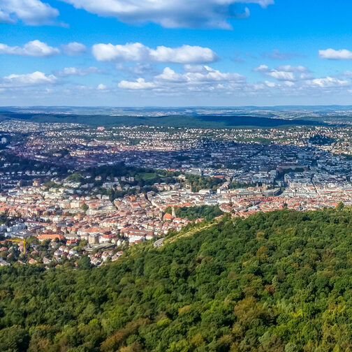 Luftaufnahme einer Stadt, im Vordergrund ist viel Wald zu sehen.
