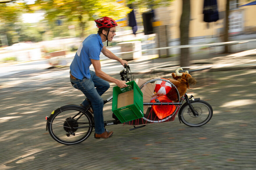 Ein Mann fährt mit einem beladenen Lastenrad über einen Platz.