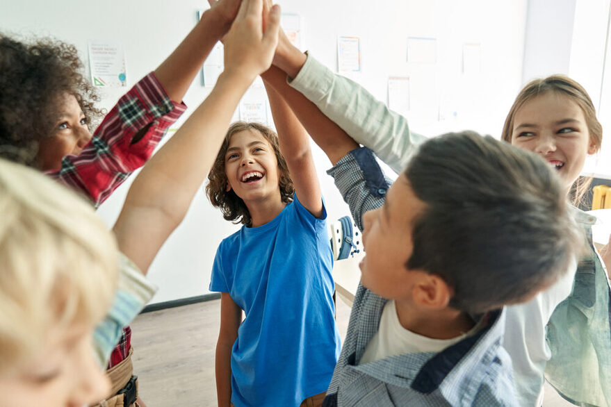 Fünft Kinder vereinen jeweils einen Arm in der Mitte zwischen sich und lächeln dabei.