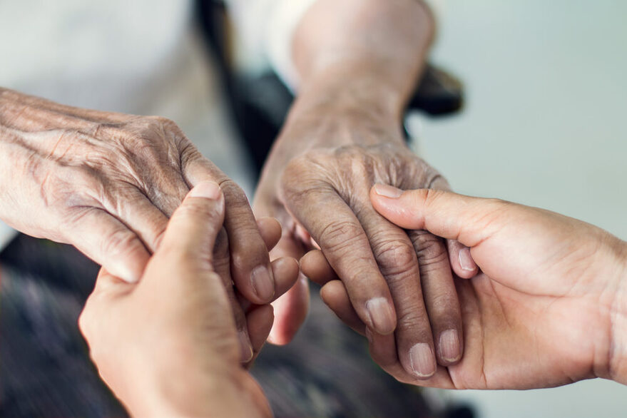 Die Hände eines jungen Erwachsenen halten die Hände einer Seniorin.