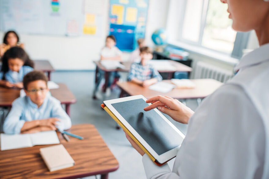 Lehrerin mit Tablet in der Hand vor ihrer Klasse.
