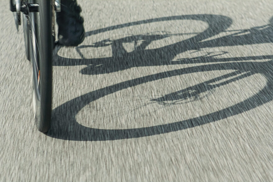 Ein Fahrrad fährt auf einer Straße und wirft einen Schatten auf diese.