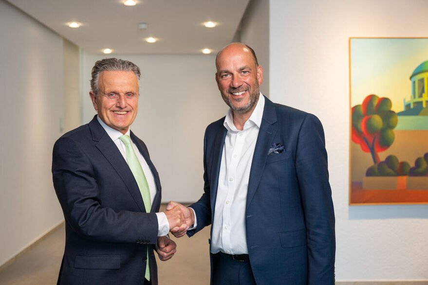 Zwei Männer geben sich die Hand und schauen dabei in die Kamera.
