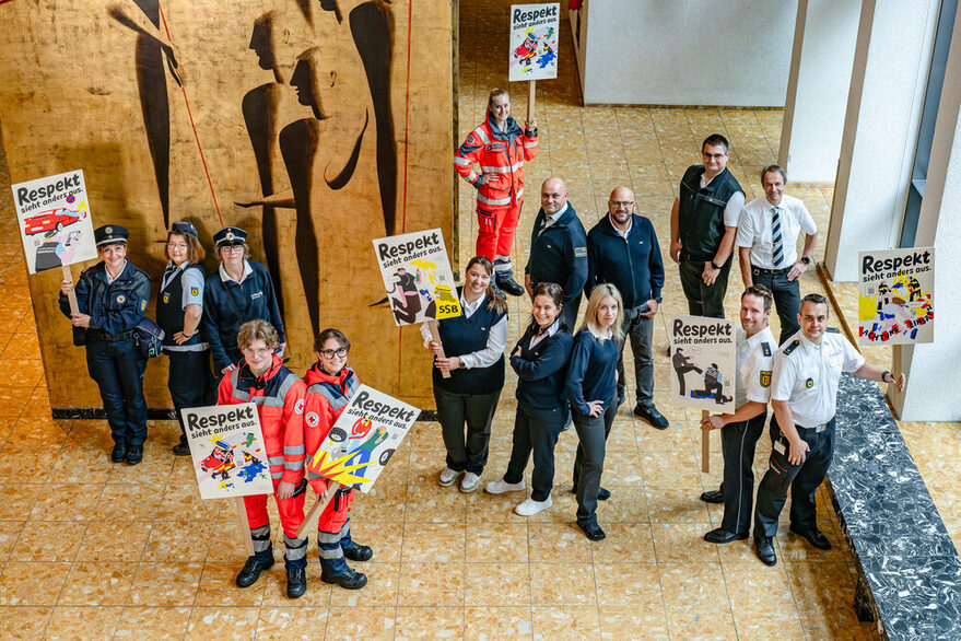 Mitarbeitende der Landeshauptstadt Stuttgart, Polizei, Deutschem Roten Kreuz, Stuttgarter Straßenbahnen AG und Johanniter halten im Foyer des Stuttgarter Rathauses die neuen Motive der Respekt-Kampagne 2025 in der Hand.