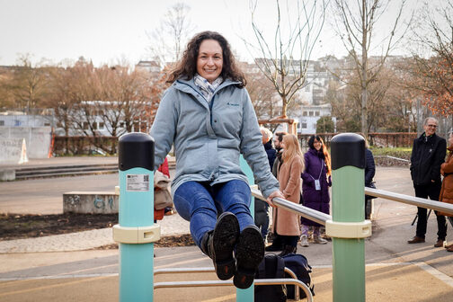 The head of the Office for Sport and Exercise, Daniela Klein, inaugurates the new calisthenics facility in Feuerbach. With her hands, she lifts herself into the air on two bars on the left and right.