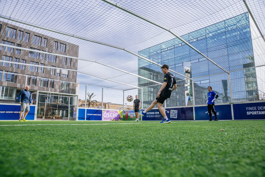 Mehrer Personen spielen Fußball auf einem Bolzplatz.
