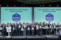 Eine Gruppe Menschen steht auf einer Bühne. Im Hintergrund der Text: Das "Bewährt vor Ort-Siegel" Verleihung 2025.