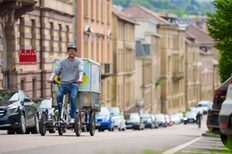 Ein junger Mann fährt gut gelaunt mit einem Lastenrad durch eine Stuttgarter Straße. Die Gebäude im Hintergrund sind unscharf, der Mann und das Rad stehen im Fokus.
