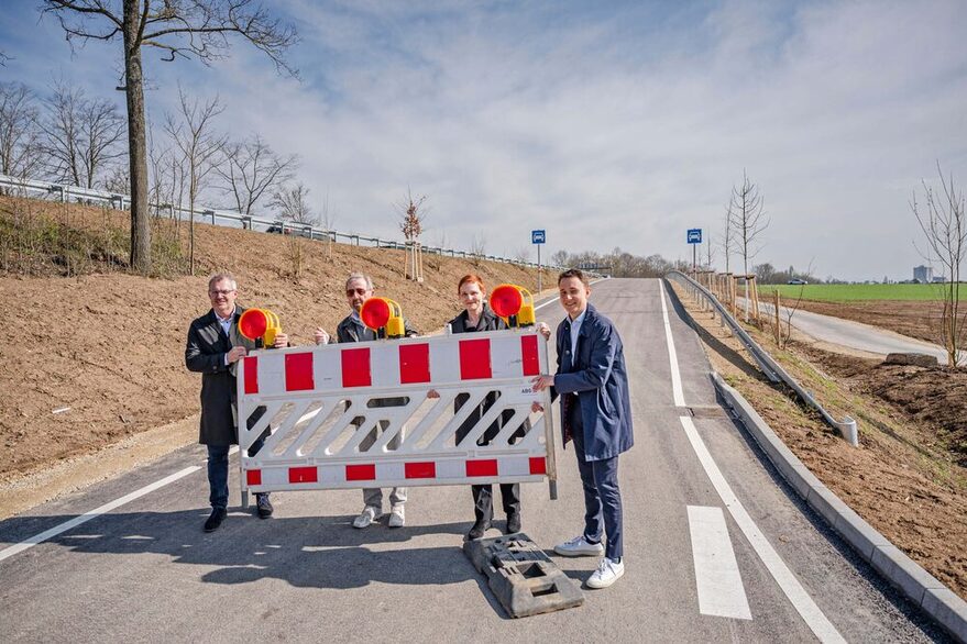 Vier Menschen heben an  einer Auffahrtsrampe eine Baustellenabsperrung an.
