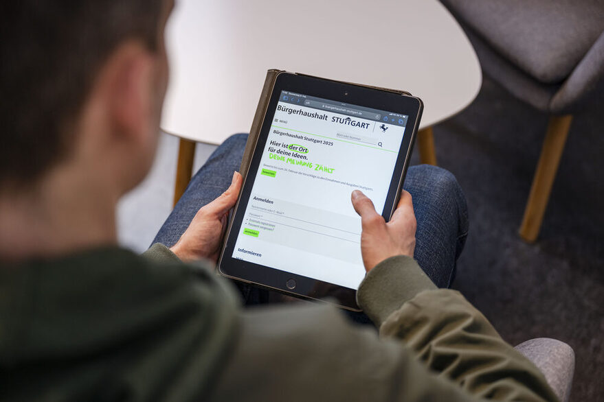 Ein Mann hält ein Tablet in der Hand. Auf dem Display ist die Seite des Stuttgarter Bürgerhaushalts geöffnet.
