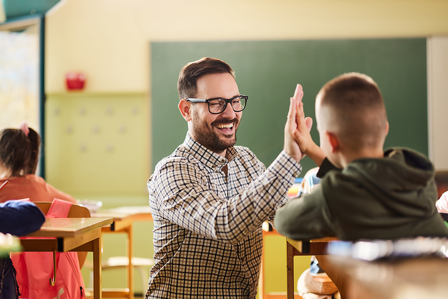 Ein Lehrer klatscht fröhlich mit einem Kind in einem Klassenzimmer ab.