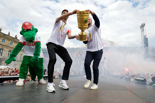 The photo shows VfB mascot Fritzle, captain Atakan Karazor and coach Sebastian Hoeneß (from left to right) with the DFB Cup in the stands on Stuttgart's Schlossplatz. Photo: Leif Piechowski/City of Stuttgart