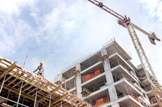 Construction site for a multi-story building with a construction worker on the roof and a crane next to it.