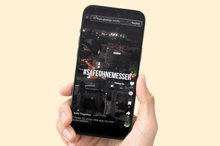 Eine Hand hält ein Handy, auf dem Bildschirm sieht man Stuttgart im Hintergrund, im Vordergrund steht #Safeohnemesser.