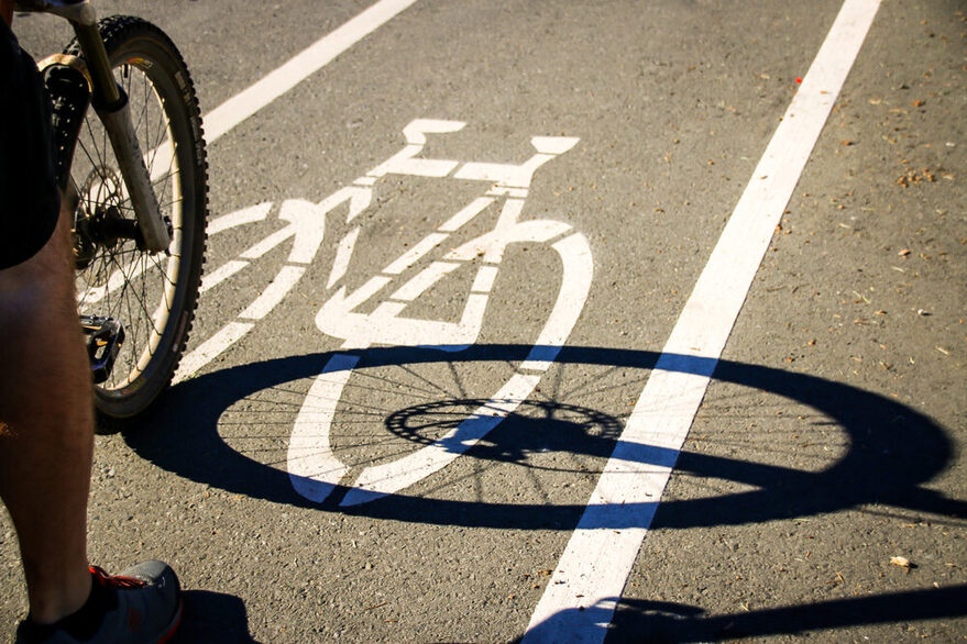 Das Vorderrad eines Fahrrads mit dem Bein eines Radfahrers ist auf einem sonnigen Fahrradweg zu sehen.